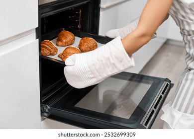 female baker taking tray with fresh croissants from oven in modern kitchen, close-up - Powered by Shutterstock