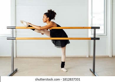 Female ballet dancer with black hair stretching her leg. Side view of young woman preparing for a ballet class in studio.