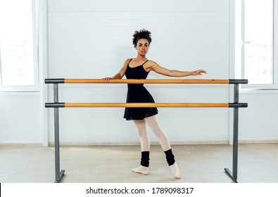Female ballet dancer with curly hair holding a barre preparing for a ballet class in a studio
