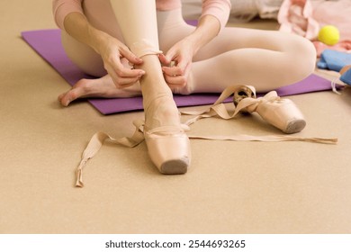 Female ballet dancer sitting on the floor, preparing pointe shoes before practice. - Powered by Shutterstock