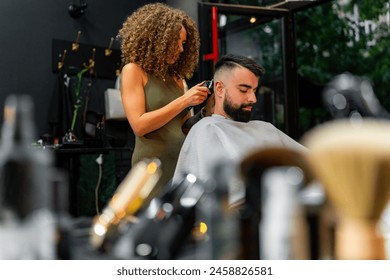 Female barber meticulously trims and styles a male client's hair with electric clippers in a modern barber shop, ensuring a precise and stylish cut. - Powered by Shutterstock