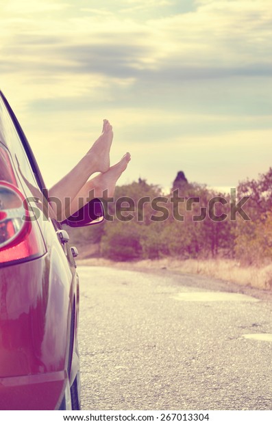 Female bare feet stick out of car window on\
mountain background. Travel\
concept.