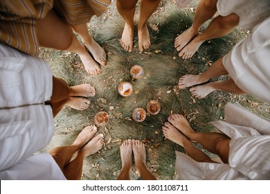Female barefoot feet on dry grass standing in a circle with glasses of wine in the middle.