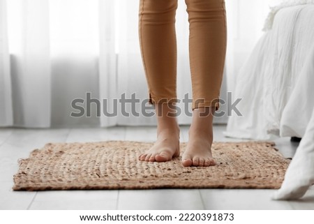 Female barefoot legs on wicker carpet in bedroom