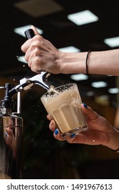 Female Barista Is Pouring Nitrogen Coffee With Blown Froth And Splashes Into A Glass On Bokeh Background