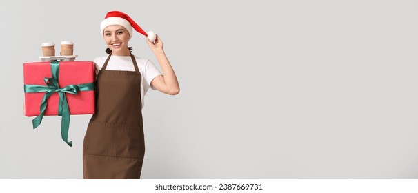 Female barista in Santa hat and with gift on light background with space for text - Powered by Shutterstock