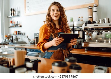 Female barista takes an order from a tablet while standing behind the counter in a coffee shop. Business, technology concept. Takeaway food. - Powered by Shutterstock