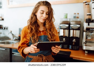 Female barista takes an order from a tablet while standing behind the counter in a coffee shop. Business, technology concept. Takeaway food. - Powered by Shutterstock