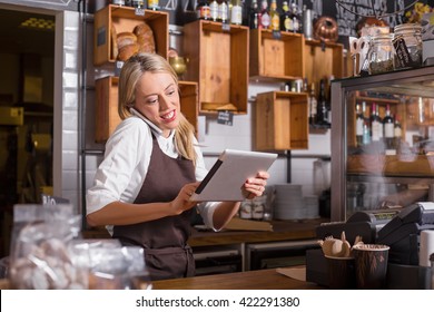 Female barista talking on the phone and using tablet while standing behind the counter
