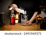 Female bartender hands scooping ice cubes into a glass for mixing cocktails