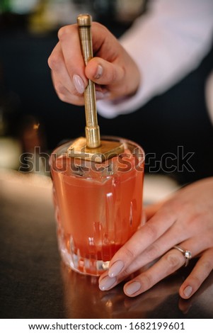 Female bartender makes a cocktail based on vodka and peach cordial in a rocks glass and puts a stamp on ice. Smooth image with shallow depth of field.