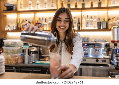 Female bartender making alcoholic cocktail on the bar counter, Young professional bartender working on a bar preparing cocktails - Powered by Shutterstock