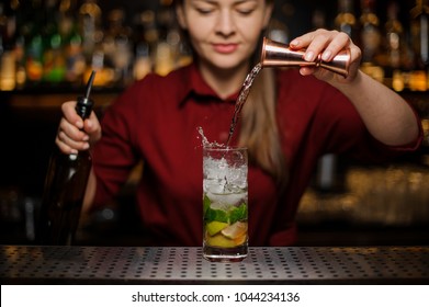 Female bartender pouring out a transparent drink from the measuring pile with splash for preparing a delicious fresh cocktail - Powered by Shutterstock