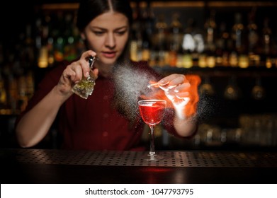 Female bartender sprinkling a cocktail glass with tasty Aperol syringe cocktail with a peated whisky and making a smoky note on the bar counter
