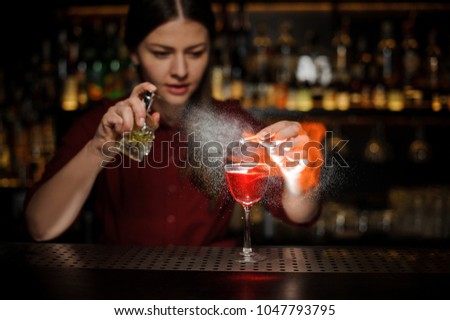 Female bartender sprinkling a cocktail glass with tasty Aperol syringe cocktail with a peated whisky and making a smoky note on the bar counter