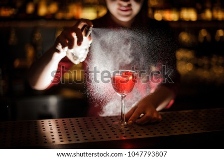 Female bartender sprinkling a cocktail glass filled with tasty Aperol syringe summer cocktail with a peated whisky on the bar counter