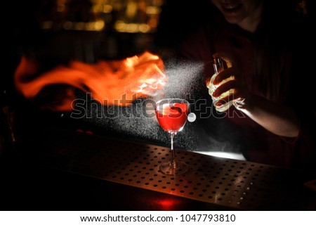 Female bartender sprinkling a cocktail glass filled with tasty Aperol syringe summer cocktail with a peated whisky and making a smoky note