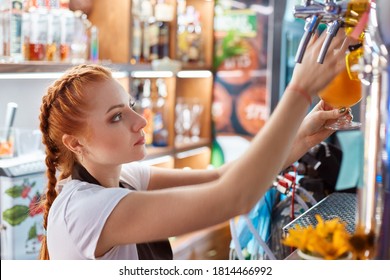 Female Bartender Tapping Craft Beer In Bar, Side View Of Red Haired Barman Wearing White Casual T Shier And Apron, Looks Serious, Being Concentrated On Her Work.
