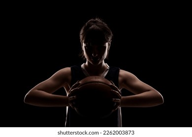 Female basketball player. Beautiful girl holding ball. Side lit half silhouette studio portrait against black background. - Powered by Shutterstock