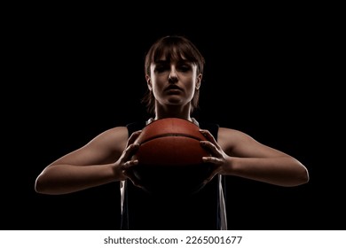 Female basketball player. Beautiful girl holding ball. Side lit half silhouette studio portrait against black background. - Powered by Shutterstock