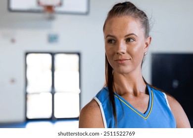 Female basketball player in blue jersey standing confidently in gymnasium, copy space. Sports, athlete, confidence, determination, uniform, competition - Powered by Shutterstock