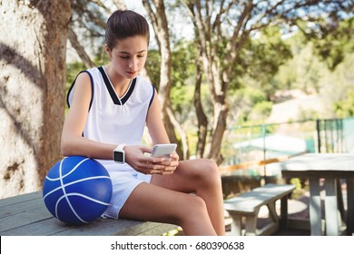 Female basketball player using mobile phone while sitting on bench in court - Powered by Shutterstock