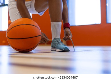 Female basketball player wearing sports clothes and tying shoes at gym, copy space. Sport, activity and lifestyle, unaltered. - Powered by Shutterstock