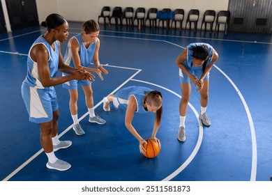 Female basketball players training, one doing push-ups with ball on court. athletes, teamwork, sports, fitness - Powered by Shutterstock