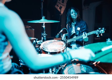 Female bass guitarist concentrating on playing her instrument while a drummer plays in the foreground during a recording session in a professional music studio - Powered by Shutterstock