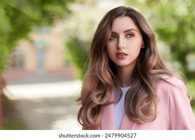 Female beauty. Beautiful girl with gorgeous long wavy hair, dressed in a pink jacket, stands against summer greenery on the city street. Copy space. Summer vacation. - Powered by Shutterstock