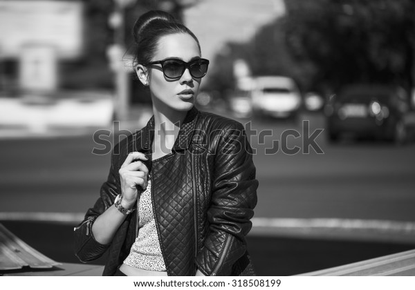 Female
beauty concept. Portrait of fashionable young girl in casual black
jeans, black jacket, white crop-top, sunglasses and small  bag
posing on the street.  Vogue style. outdoor
shot