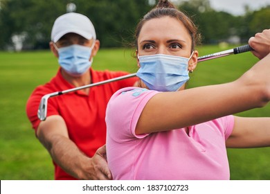 Female beginner golfer in a face mask mastering the downswing technique supported by her coach - Powered by Shutterstock