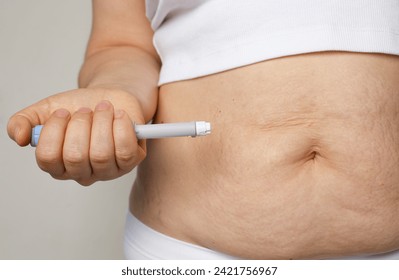 Female belly and hand closeup with Semaglutide Injection pen or insulin cartridge pen. Medical equipment for diabetes patient. Diabetes and weight loss concept.  - Powered by Shutterstock