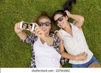 Female best friends lying on the grass and taking selfies - Powered by Shutterstock