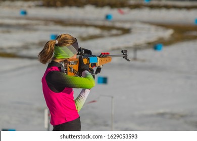 Female biathlon racer is standing on the ground and aiming her rifle. Biathlete woman on a shooting range, firing standing up.