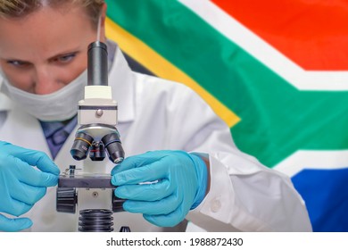 Female Biochemist Looking Through A Microscope Against South Africa Flag Background. Medical Technology And Pharmaceutical Research And Development Of Science Concept In South Africa