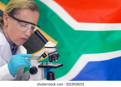 Female Biochemist Mixing Substances To Study Under The Microscope Against South Africa Flag Background. Medical Technology And Pharmaceutical Research, Development Of Science Concept In South Africa