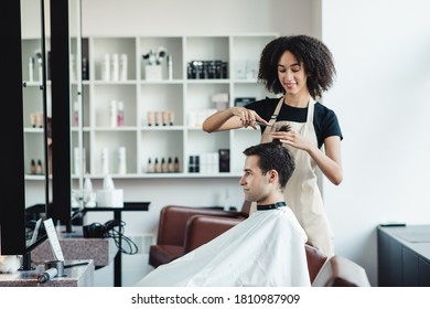 Female black barber cutting hair of young man client, hairdresser salon interior, free space - Powered by Shutterstock