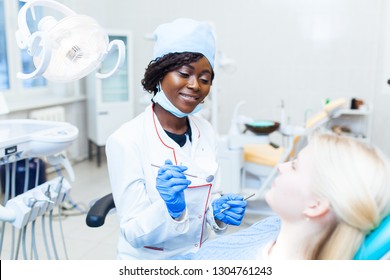 Female black dentist in dental office talking with female patient and preparing for treatment. Modern medical equipment - Shutterstock ID 1304761243