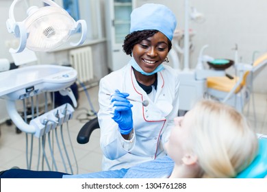 Female black dentist in dental office talking with female patient and preparing for treatment. Modern medical equipment. Dental clinic concept - Shutterstock ID 1304761288