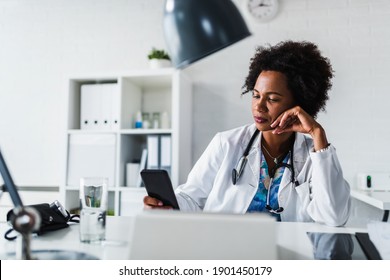 A Female Black Ethnicity Doctor Sits At Her Office And Using Mobile Smart Phone