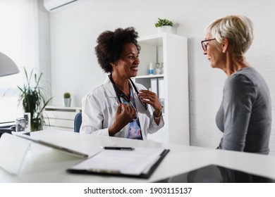 A Female Black Ethnicity Doctor Sits At Her Office And Examining Elderly Female Patient