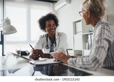 A Female Black Ethnicity Doctor Sits At Her Office And Talking With Elderly Female Patient