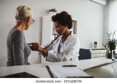 A Female Black Ethnicity Doctor Sits At Her Office And Examining An Elderly Female Patient. Heart Examination.