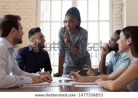 Female black executive leader talking to happy diverse employees group at corporate office briefing, multiracial coworkers listening to african woman boss explain new strategy plan at team meeting