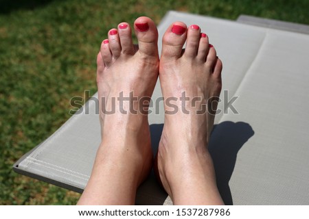 Female with black leather gladiator sandals enjoying the sun in a deckchair. The female has painted her toenails bright pink. Photographed during a sunny summer day on a vacation.