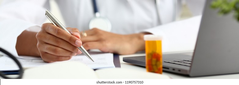 Female Black Medicine Doctor Hand Hold Jar Of Pills And Write Prescription To Patient At Worktable. Panacea And Life Save, Prescribing Treatment Legal Drug Store Concept. Empty Form Ready To Be Used