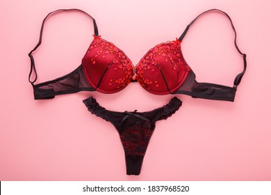 Female black red bra and string panties on light pink table background. Pastel color. Daily underwear. Closeup. 