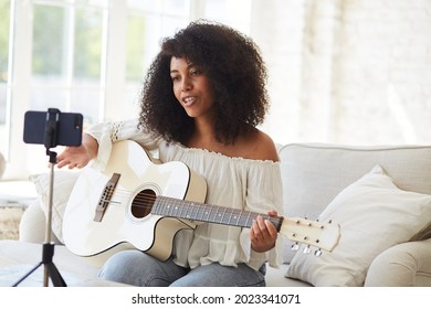 Female black vlogger influencer playing guitar and recording tutorial, young woman blogger greets fans and teaching play songs and instrumental music online lessons, Online music concert from home. - Powered by Shutterstock