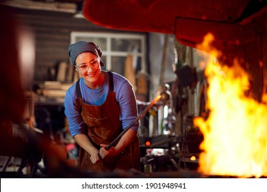 Female Blacksmith Heating Metalwork In Flames Of Forge - Powered by Shutterstock